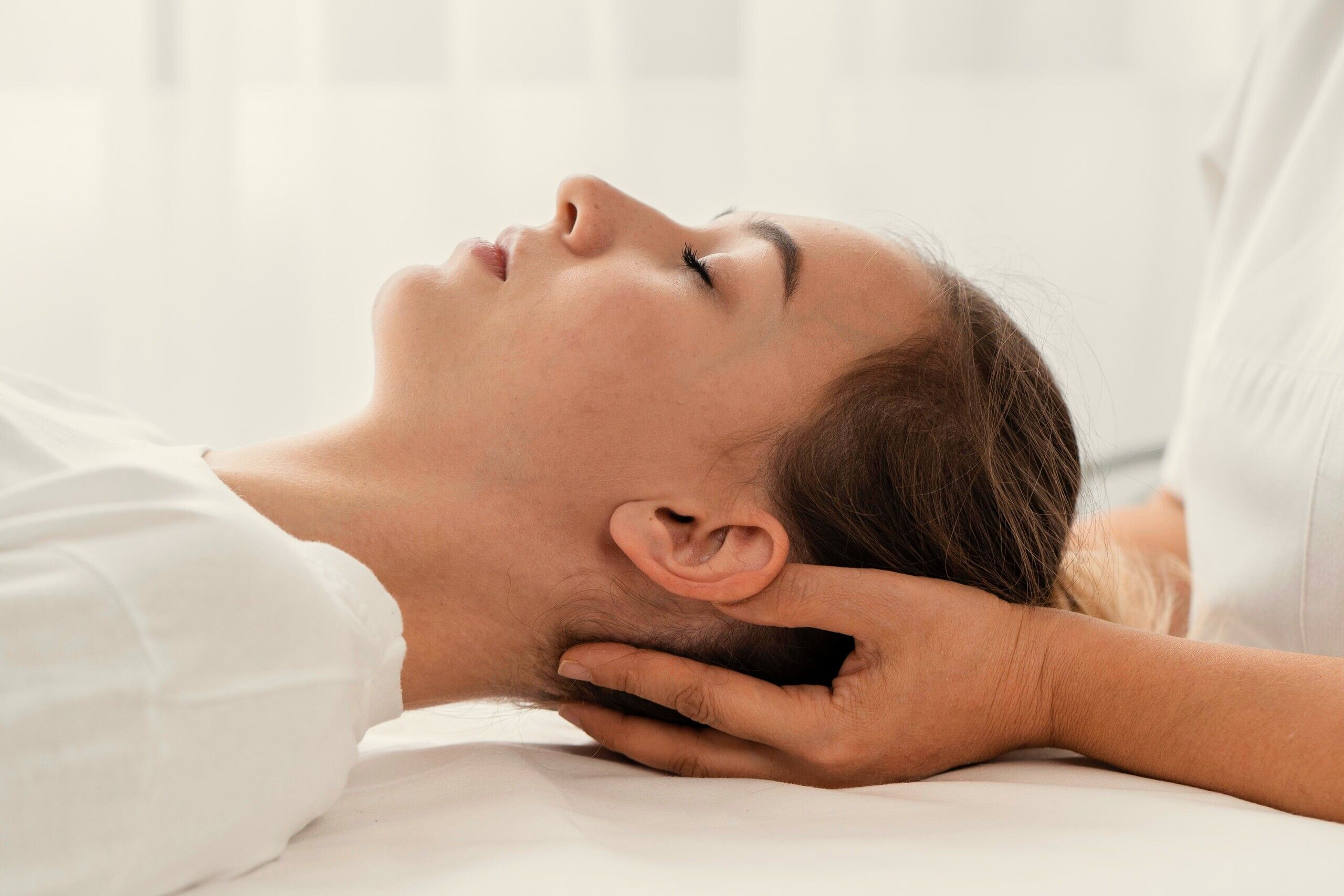 A therapist’s hand cradling the back of the neck of a woman lying face up with her eyes closed