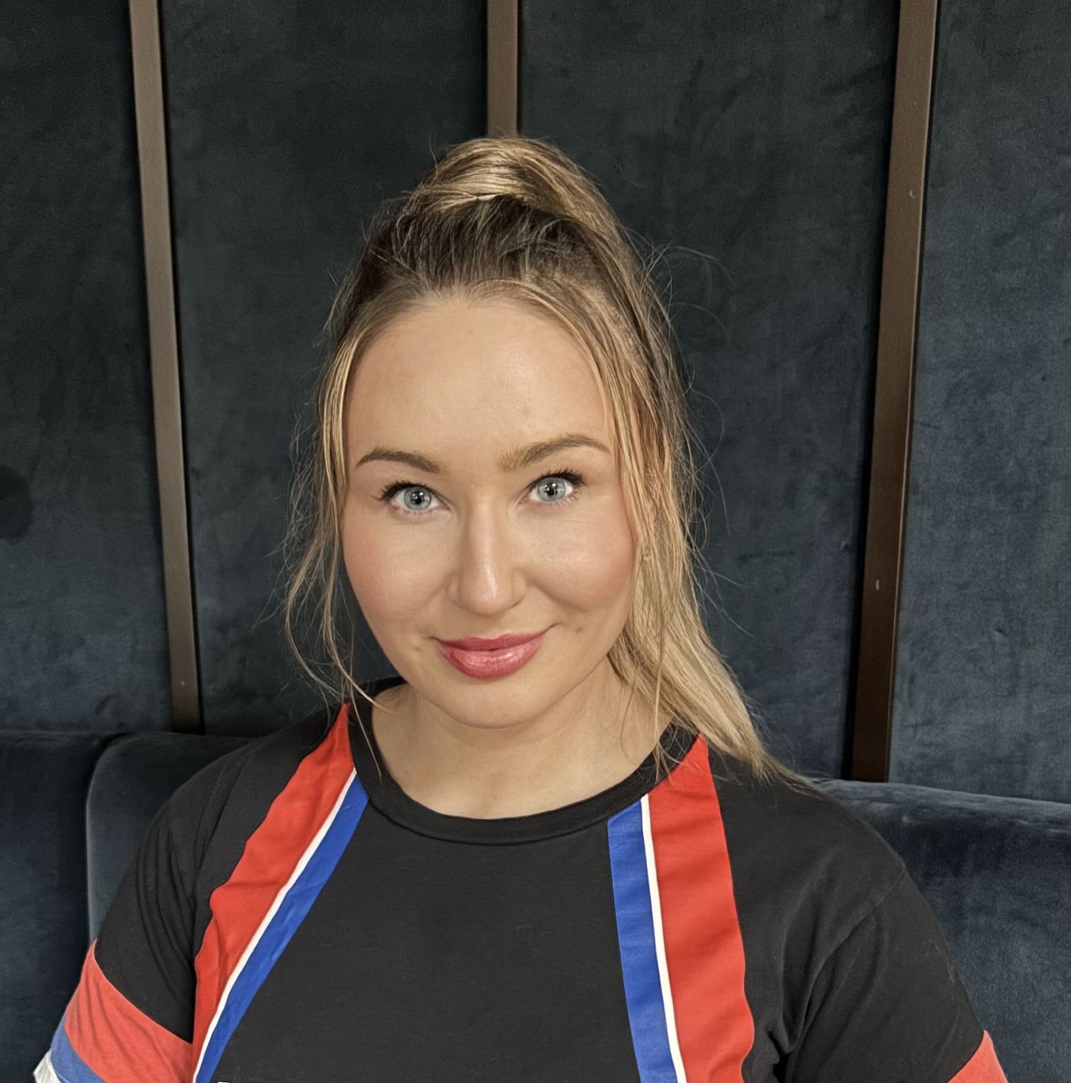 Violeta Barbolyuk in a black T-shirt with red, white and blue stripes, facing the camera, in front of dark velvet wall panels