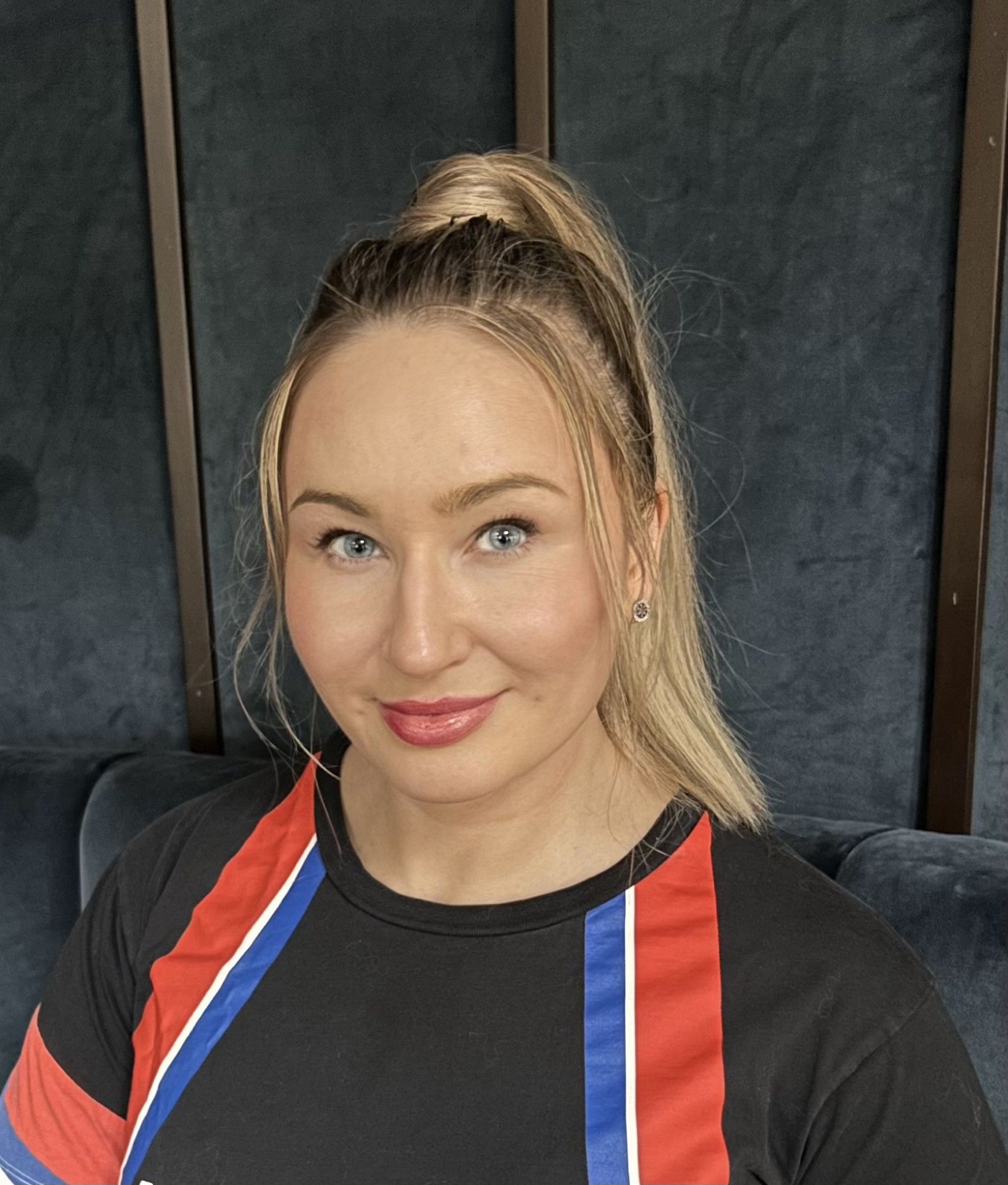 Violeta Barbolyuk smiling in a black athletic T-shirt with red, white and blue stripes, dark velvet panels with bronze strips behind her