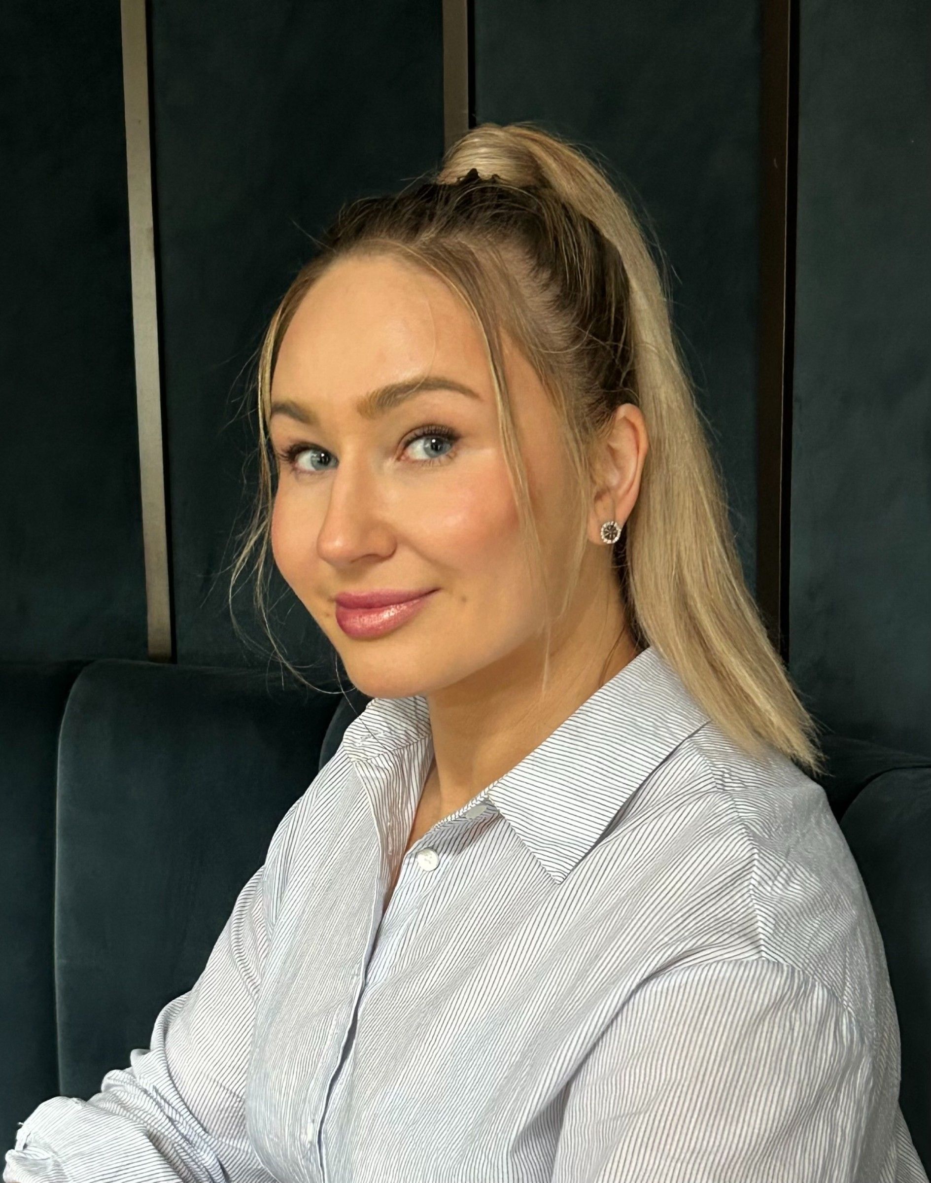 Violeta Barbolyuk in a light pinstriped shirt, seated on a dark velvet sofa and turned toward the camera
