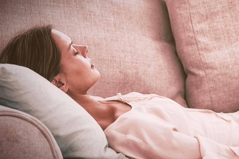 A woman resting on a pink sofa with her eyes closed, her head on a pillow